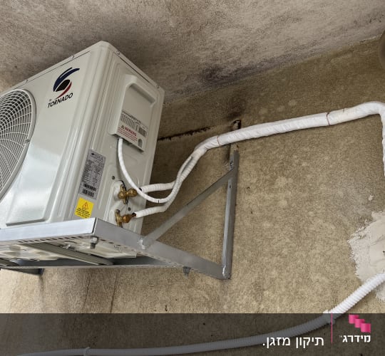 יחידת מיזוג אוויר חיצונית מותקנת על קיר עם צינורות מחוברים